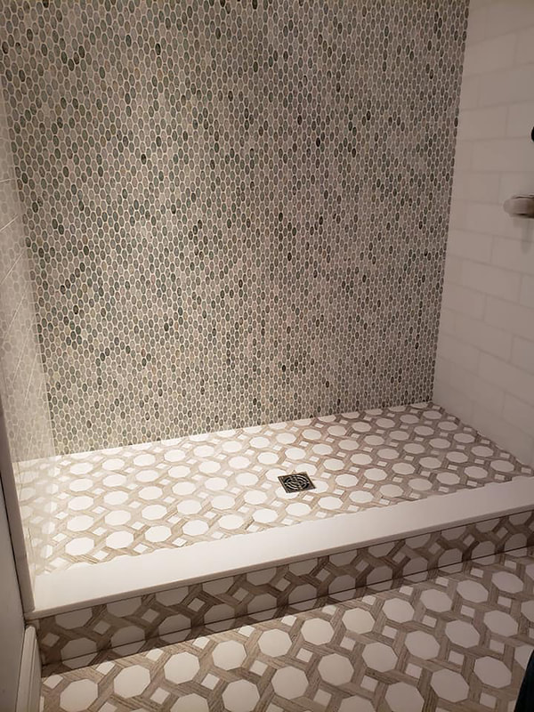 White marble hexagon tile with wood look tile details on floor, blue glass and subway tile shower