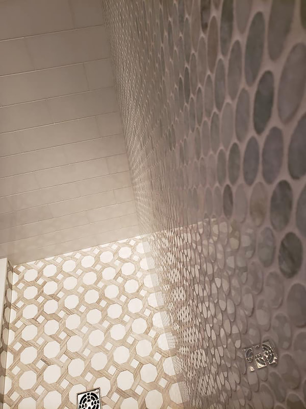 Close up of White marble hexagon tile with wood look tile details on floor, blue glass and subway tile shower