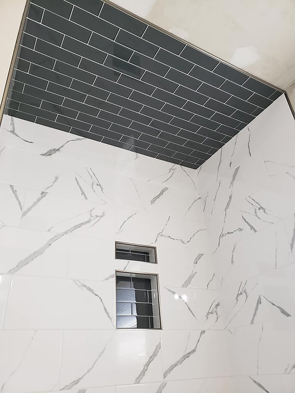 White marble shower with shower niche and black subway tile ceiling