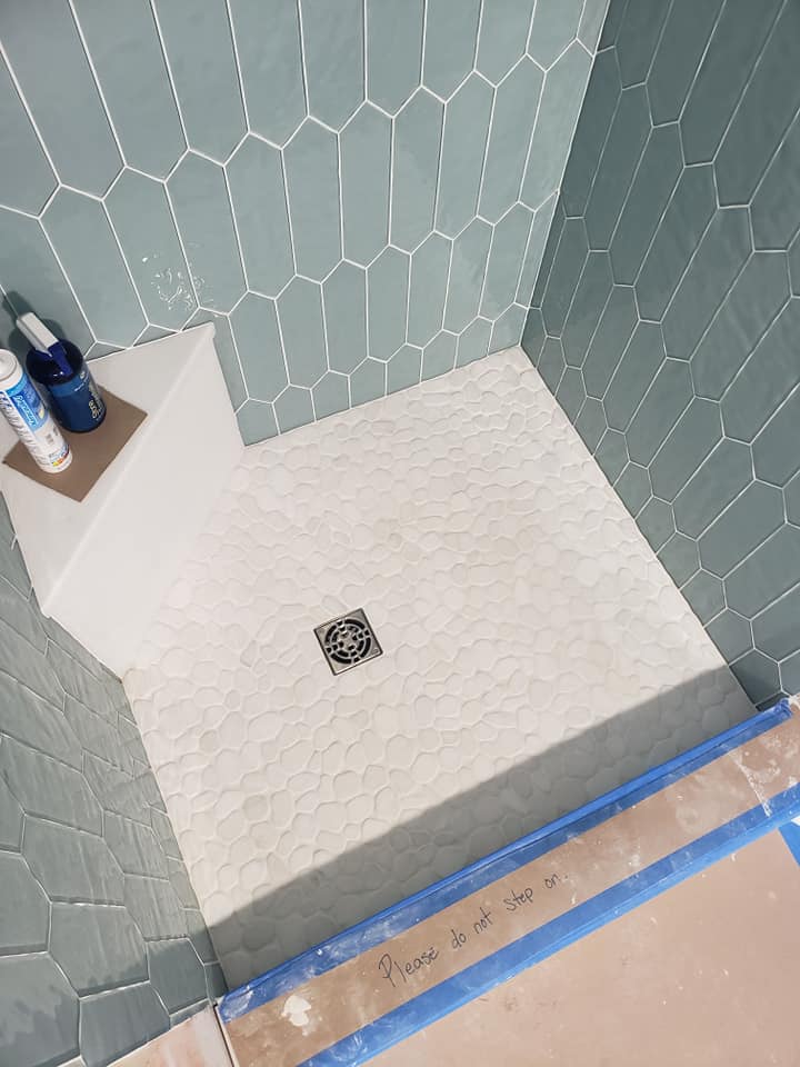 Completing custom shower with ice glass tile and white pebble floor