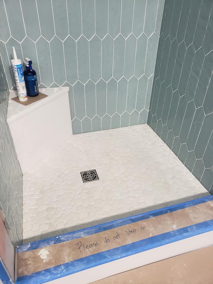 Completing custom shower with ice glass tile and white pebble floor